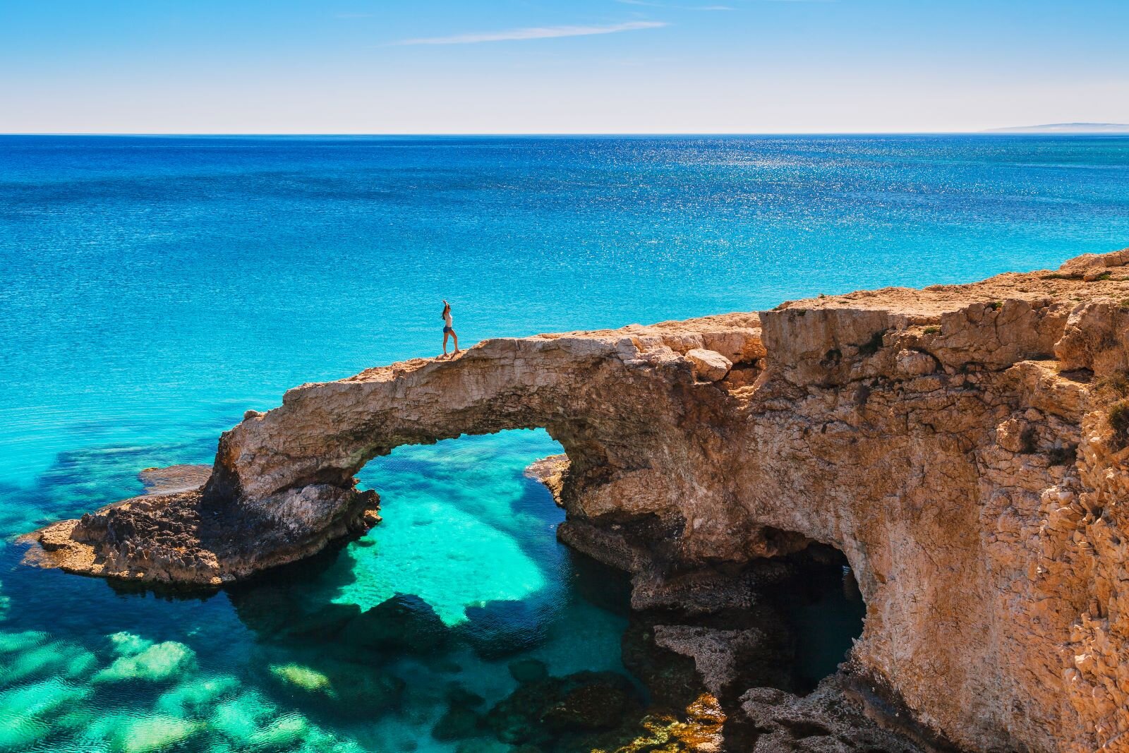 Kobieta stojąca na łuku skalnym na Cape Greco na Cyprze, w tle niebieskie morze