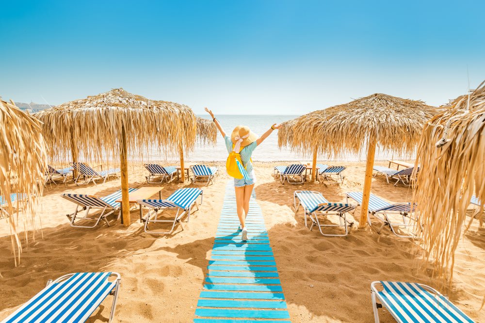 kobieta na plaży z leżakami unosi ręce w geście radości z wakacji